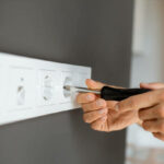 Electrician mounting electric sockets on the grey wall at home